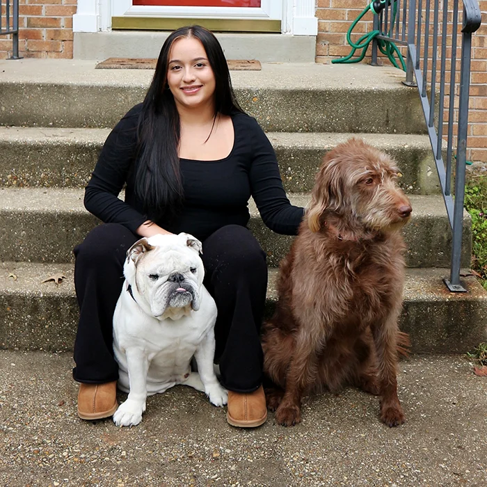 Narda sitting on outdoor steps with an English bulldog on her left and a large brown dog on her right.