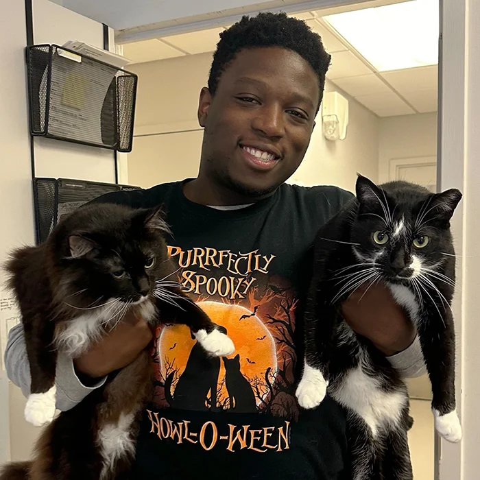 Raphy smiling while holding two black and white cats.